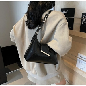 Detail der schwarzen Lackleder-Hobo-Tasche mit goldenem Metallstreifen an einer Person