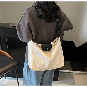 Detail of the white oversized hobo bag showing the black leather flap and adjustable strap
