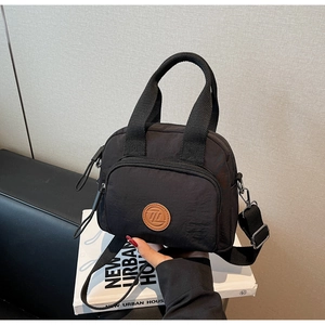 Nahaufnahme der schwarzen Nylon-Umhängetasche mit Lederlogo auf einem Buchhintergrund