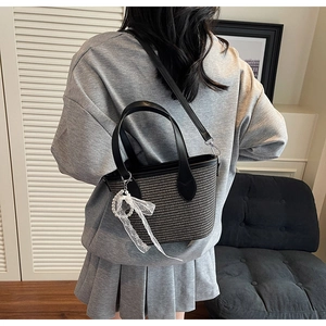 Détail du sac bandoulière en paille tissée avec breloque nœud en dentelle et perles