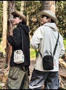 Outdoor drawstring bucket bags in black and beige shown in a forest setting