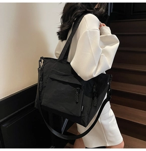 Detail of black nylon tote bag featuring front zipper pocket and adjustable shoulder strap