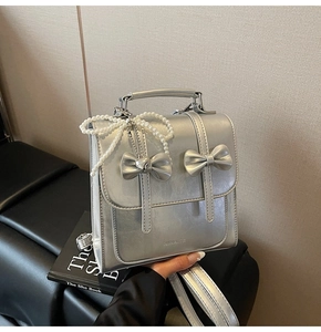 Détail d'un sac à dos argenté avec des nœuds décoratifs et un pendentif en perles