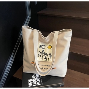Detail of beige canvas tote bag featuring Moon and Sixpence art on wooden stairs