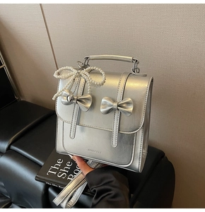 Détail d'un sac à dos argenté métallisé avec nœuds en cuir et pendentif perle papillon