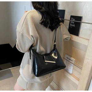 Detail einer glänzenden schwarzen Lackleder-Schultertasche mit eleganter goldener Metallschnalle