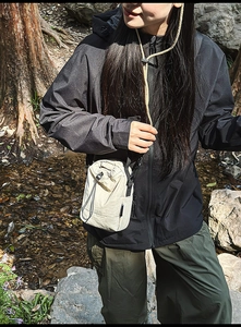 Beige lightweight drawstring crossbody bag worn by a model in a forest hiking scene