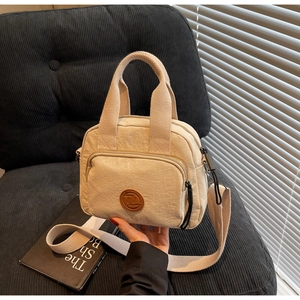 Detail der beige Falten-Nylontasche mit rundem braunem Leder-Logo-Patch vorne