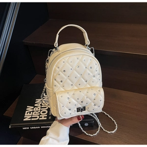 Detailed close-up of quilted off-white mini backpack with diamond accents and chain strap