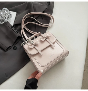 Détail du sac élégant en cuir beige avec double nœuds, perles et pendentif cœur