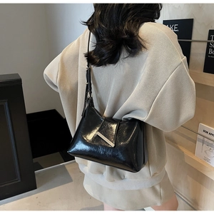 Detail einer schwarzen glänzenden Hobo-Tasche aus Retro-Ölleder mit Metallleiste am Modell