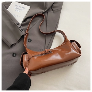 Detail of dark brown glossy leather dumpling bag with side pocket on grey blazer