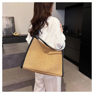 Grand sac cabas en paille avec bordure en cuir noir porté par un mannequin dans une pièce