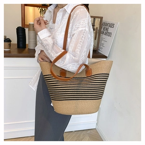 Détail montrant le sac cabas en paille à rayures noires et anses en cuir marron