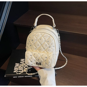 Detail of cream quilted mini backpack with rhinestones and chain strap on books