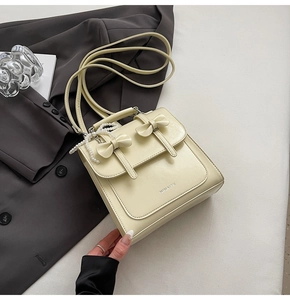 Détail du sac à main carré jaune crème avec nœuds et pendentif perle sur un costume gris