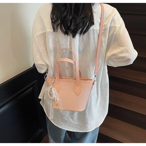 Détail du sac bandoulière en paille tressée rose avec breloque perle et nœud en dentelle