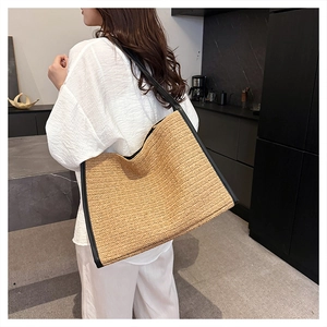 Détail d'un sac cabas en paille avec bordures en cuir noir et bandoulière contrastée
