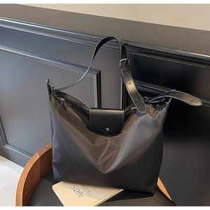 Detail shot of black nylon tote bag showing leather flap and durable metal hardware
