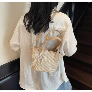 Détail du sac seau en paille tissée avec nœud en dentelle blanche et charme perlé