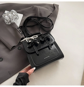 Détail du sac à main noir brillant avec nœuds, anse en perles et logo NINAITE sur tissu gris