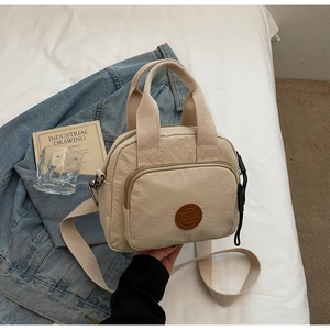 Detail einer beigen Canvas-Handtasche mit Logo auf einem Bett, zeigt das lässige Design