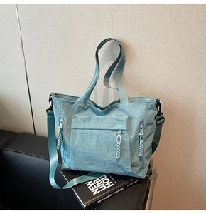 Detailed view of pale blue nylon tote bag showing flap pocket and tassel zipper pulls