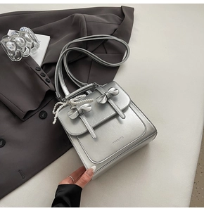 Détails d'un sac à main argenté avec des nœuds 3D et une chaîne décorative en perles