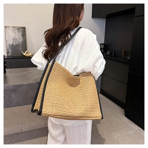 Détail d'un grand sac cabas en paille avec anses noires porté par un mannequin