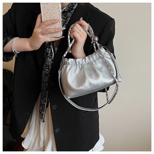Détail du sac plissé argenté métallisé avec poignée tressée et finition en cuir texturé