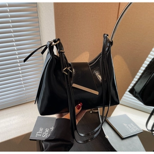 Detail einer schwarzen Lackleder-Schultertasche mit goldener Metallschnalle und Glanz