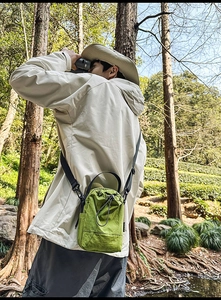 Close-up of grass green drawstring crossbody bag worn in a scenic forest setting