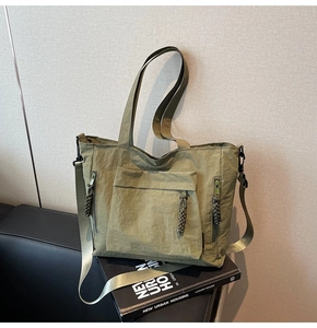 Detail of olive green nylon tote bag featuring front zip pocket and woven zipper pulls