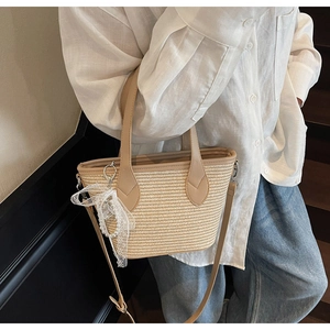 Détail d'un sac cabas en paille tressée avec bordure en similicuir, ruban et chaîne de perles