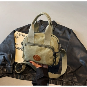 Detail einer salbeigrünen Nylon-Handtasche mit Gurt vor schwarzem Lederjacken-Hintergrund