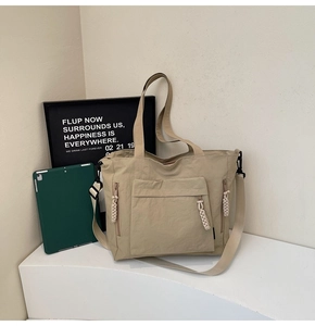 Detail of beige nylon tote bag with side zipper pockets and woven rope zipper pulls