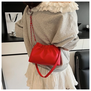 Gros plan d'un sac à main rouge motif litchi avec design plissé et bandoulière chaîne
