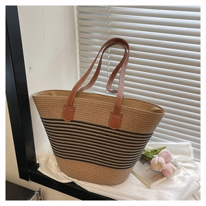 Détail du sac cabas tissé avec rayures noires et poignées en cuir marron près de la fenêtre