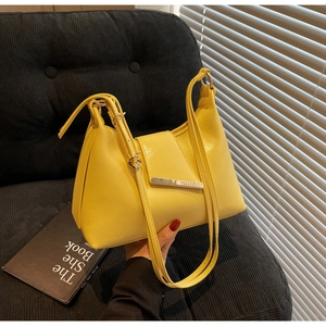 Detail einer hellgelben Leder-Achseltasche mit silbernem Metallstab auf schwarzem Sofa