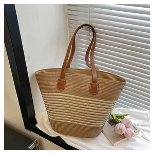 Détail d'un sac cabas en paille tressée avec anses en cuir marron et rayures