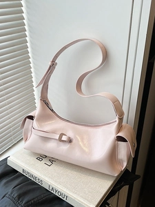 Pink glossy leather shoulder bag with adjustable strap and silver buckles on a book