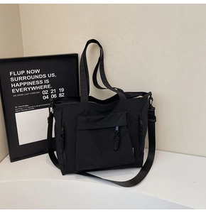 Detail view of durable black nylon tote bag showing front zip pocket and adjustable strap
