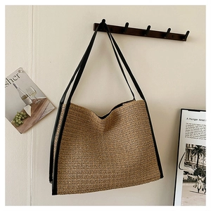 Détail du sac cabas en paille tissé main avec bandoulières noires suspendu au mur