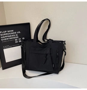 Detail of black nylon tote bag featuring front flap pocket and woven drawstring accents