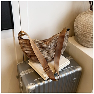 Close-up of a woven khaki straw hobo bag with a brown strap on a travel suitcase