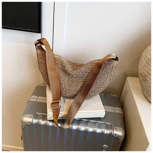 Detailed close-up of woven straw crescent bag with brown nylon strap on minimalist prop
