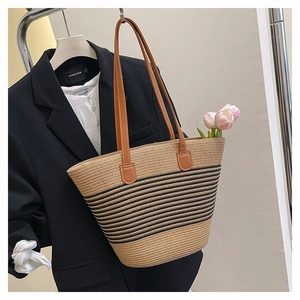 Détail du sac cabas tissé avec rayures noires et anses en cuir marron dans un décor