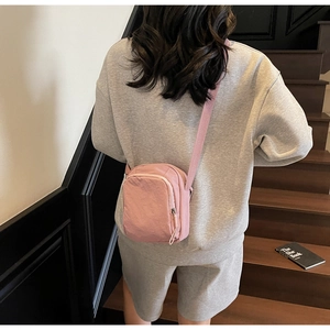 Detail einer pinkfarbenen Nylon-Umhängetasche an einem Modell vor minimalistischem Hintergrund