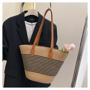 Détail d'un sac cabas en paille tissée avec rayures noires et fines anses en cuir brun