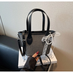 Détail du sac seau tissé avec poignées en cuir et breloque nœud en perles et dentelle